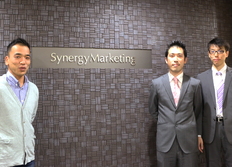 Synergy Marketingの受付の前で長谷川氏 長井氏 本多氏が立っている写真
